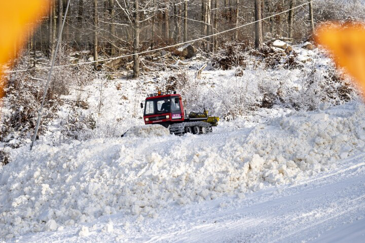 En röd pistmaskin som kör i en snöig backe.