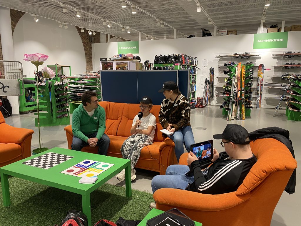 Reportrarna intervjuar. De sitter i en stor orange soffa.